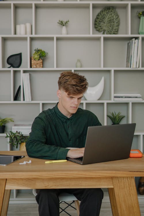 A Male Student in Green Long Sleeves Using a Laptop on a Wooden Desk