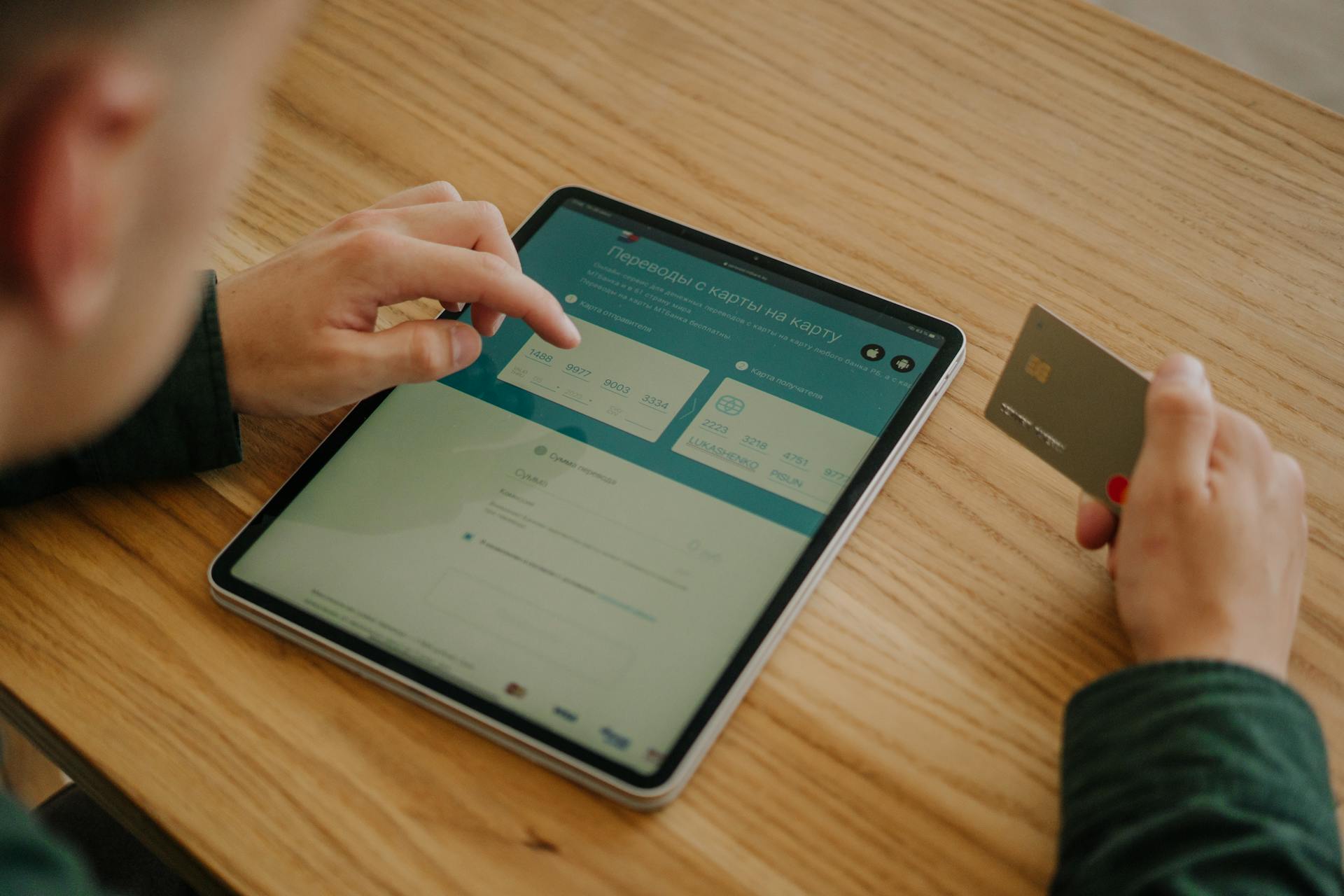 Person making an online payment using a tablet and credit card on a wooden desk.