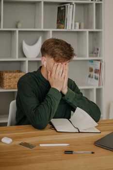 一名穿着绿色衬衫的成年男子坐在办公桌前，手拿笔记本和笔，面露压力，象征着工作场所的压力