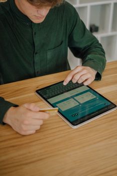 Close-up of man using a tablet and credit card for an online transaction on a wooden desk indoors.