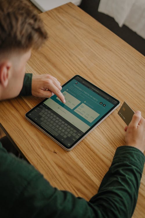 Free An adult male using a tablet and credit card for online shopping at a wooden desk indoors. Stock Photo