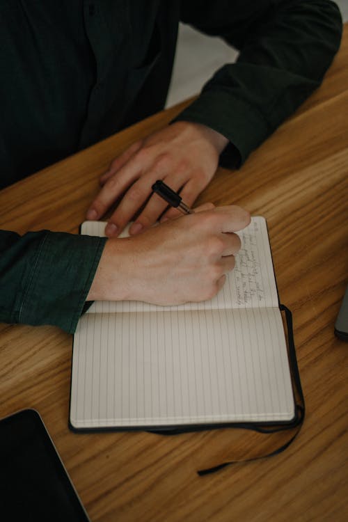 Free Close-Up Shot of a Person Writing on a Notebook on a Wooden Desk Stock Photo
