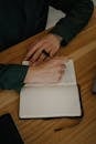Close-Up Shot of a Person Writing on a Notebook on a Wooden Desk