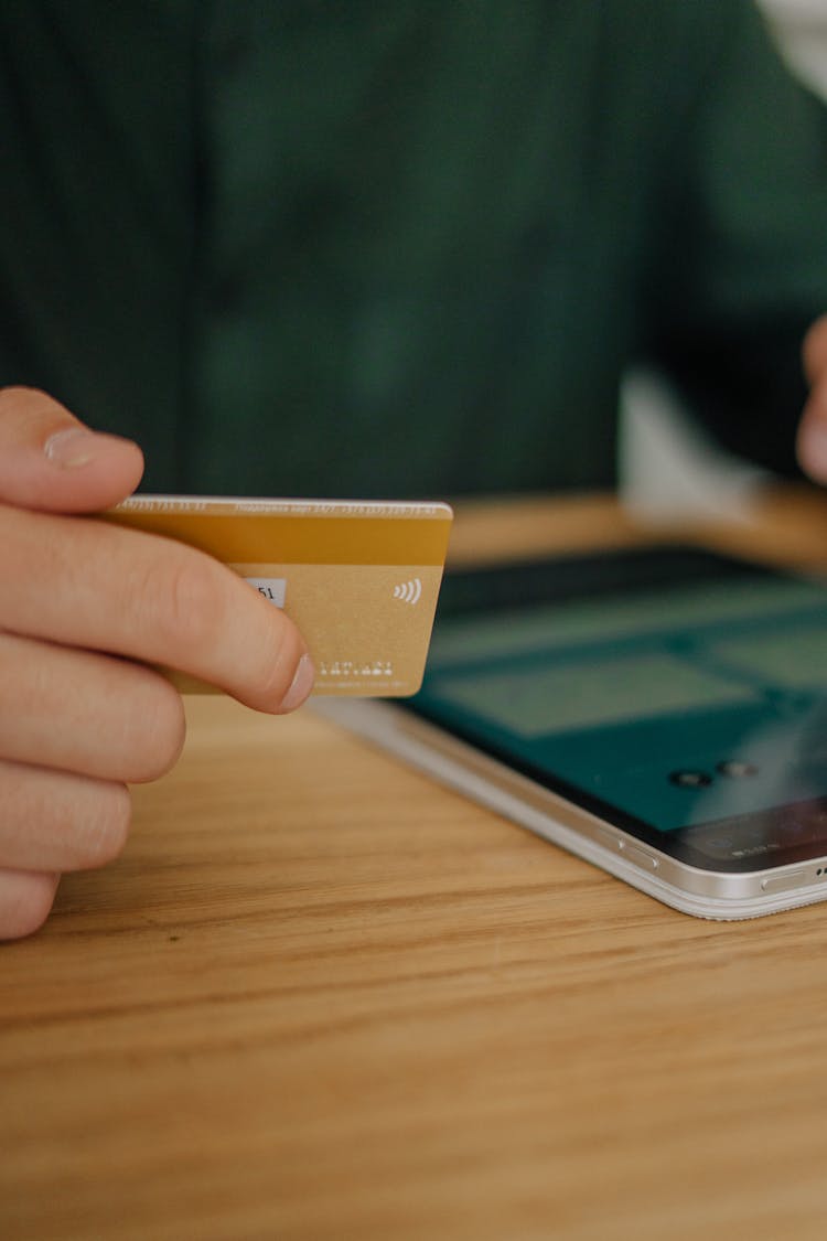 Close-Up Shot Of A Person Using An Ipad While Holding A Credit Card