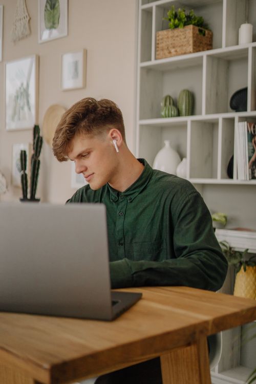 Free Young man focused on laptop work, wearing earphones, in a stylish home office space. Stock Photo