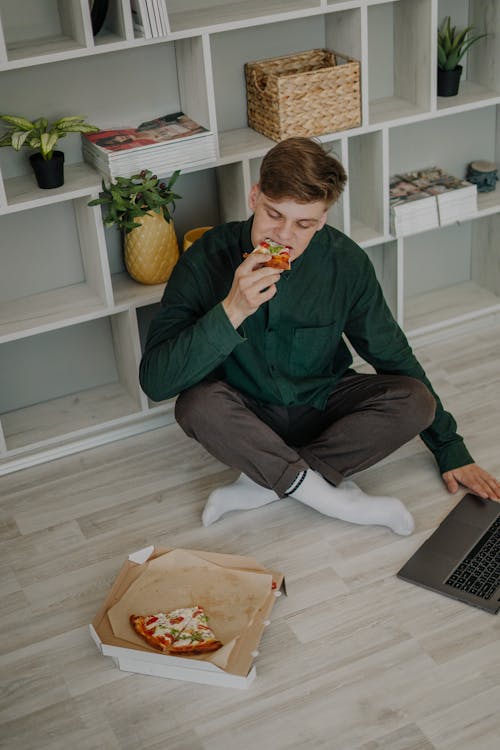 Free A Man Sitting on the Floor Eating a Slice of Pizza Stock Photo
