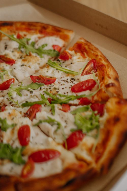 Free Mouth-watering mozzarella pizza topped with fresh cherry tomatoes and arugula in a cardboard box. Stock Photo
