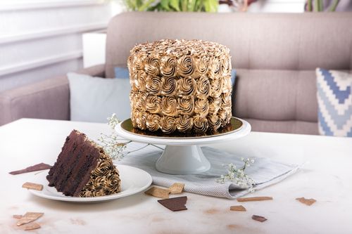 Free Rich chocolate mousse cake with swirled icing and sliced piece on a white table—ideal dessert photo. Stock Photo