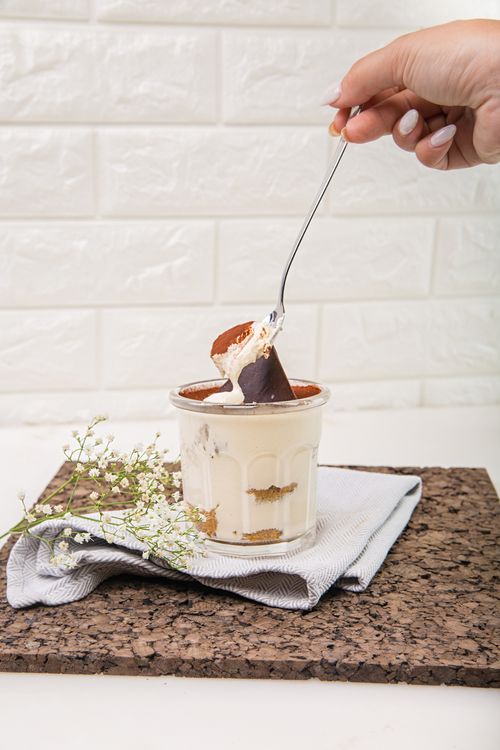Free A close-up of a creamy tiramisu dessert topped with cocoa and chocolate, accented by baby's breath flowers. Stock Photo