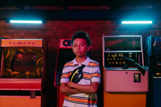 Portrait of a serious teenager in a neon-lit arcade with vintage games.
