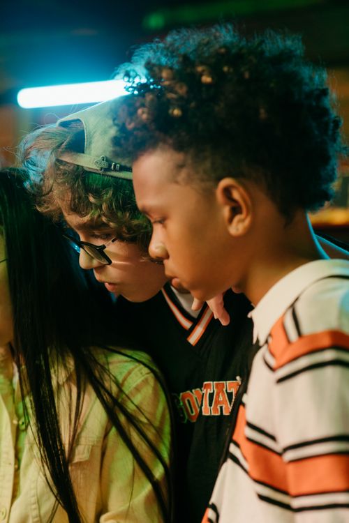 Free A diverse group of teenagers engaged in a focused discussion indoors under neon lights. Stock Photo