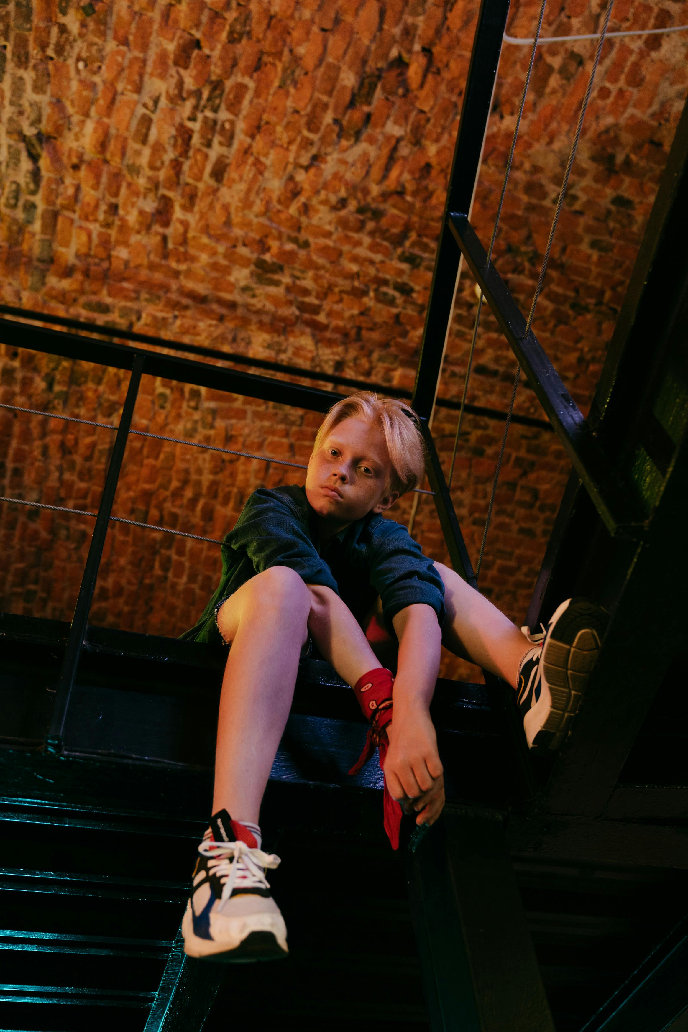 一名金发青少年坐在室内砖砌天花板的金属结构上