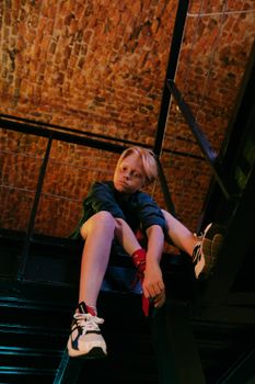 一名金发青少年坐在室内砖砌天花板的金属结构上