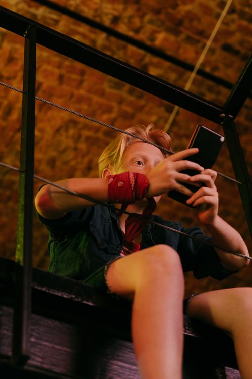 Free Low angle view of a blonde teenager using a smartphone indoors against a brick background. Stock Photo