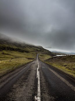 A desolate road cuts through a foggy mountainous landscape with a dramatic gray sky.