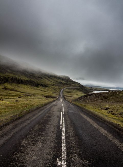A desolate road cuts through a foggy mountainous landscape with a dramatic gray sky.