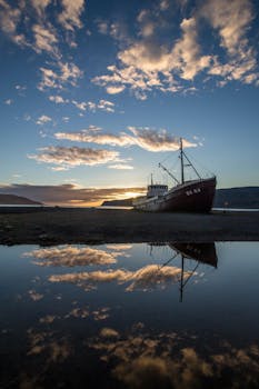 一艘船停在岸边，在平静的水面上完美地倒映着令人惊叹的日落