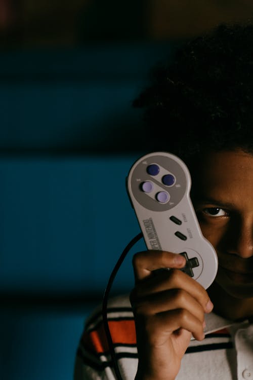 Ritaglia L'uomo Di Colore Che Mostra Il Gamepad Retrò Nell'oscurità