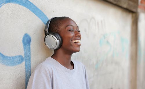 Woman with Short Hair Leaning against a Wall with Headphones and Smiling