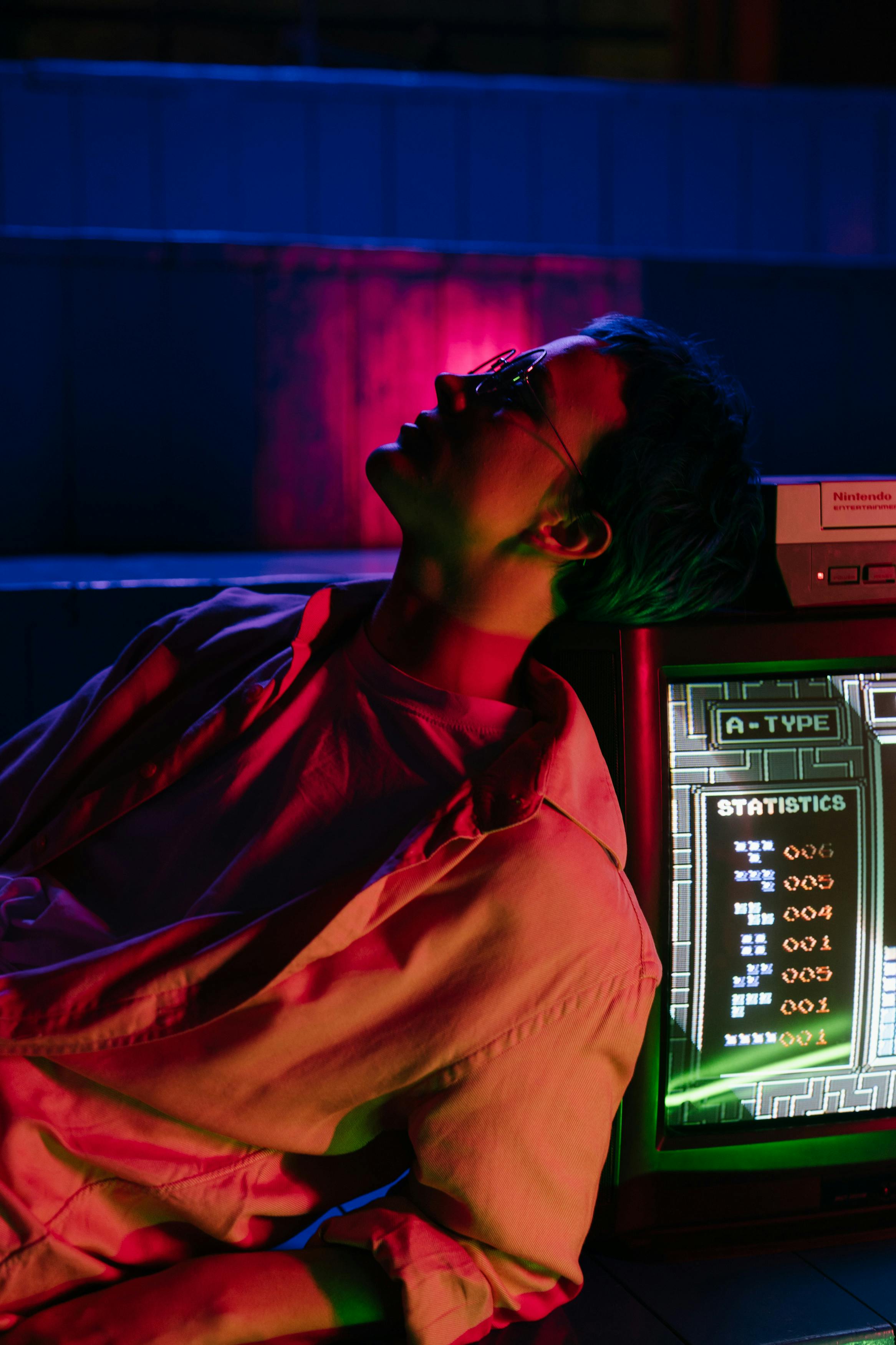 A teenager leans against a vintage arcade machine under colorful neon lights, evoking an 80s vibe.