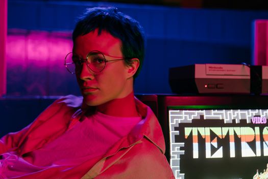 A teenager with eyeglasses in an 80s-style arcade displaying a Tetris game on screen.