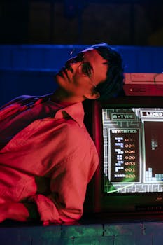 A teenager wearing eyeglasses plays a vintage video game console under neon lights.