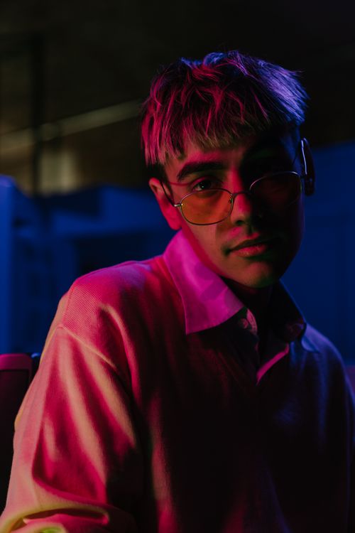 Free Portrait of a stylish teenage boy with neon lighting, wearing eyeglasses indoors. Stock Photo