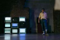 Man in Yellow Polo Shirt and Blue Denim Jeans Standing Near Black Flat Screen Computer Monitors