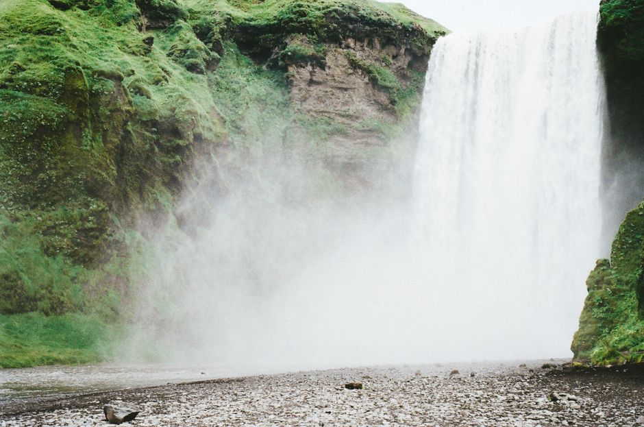 A powerful waterfall cascading over lush green cliffs, surrounded by mist.