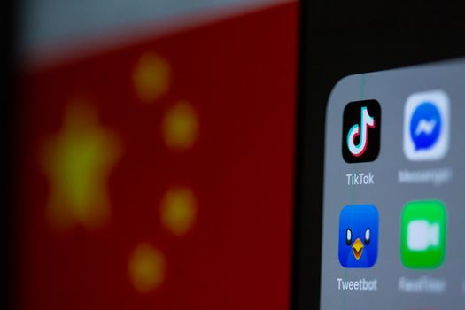 Close-up of a smartphone with popular social media app icons and blurred Chinese flag background.