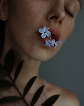 一个女人的诗意特写，嘴唇上长着丁香花，周围被树叶包围