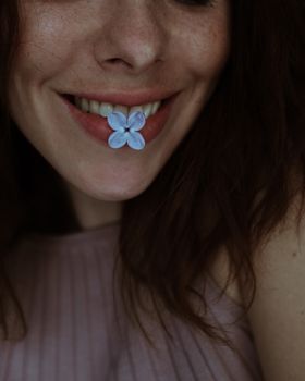 一张特写肖像中，一位微笑的女子唇间衔着一朵精致的丁香花