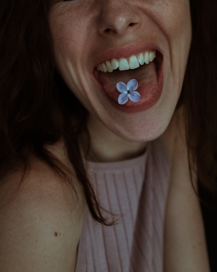 Close-Up Shot Of A Woman With Lilac Flower On Her Tongue