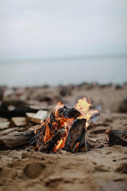 A cozy campfire burning on a sandy beach with ocean waves in the background.