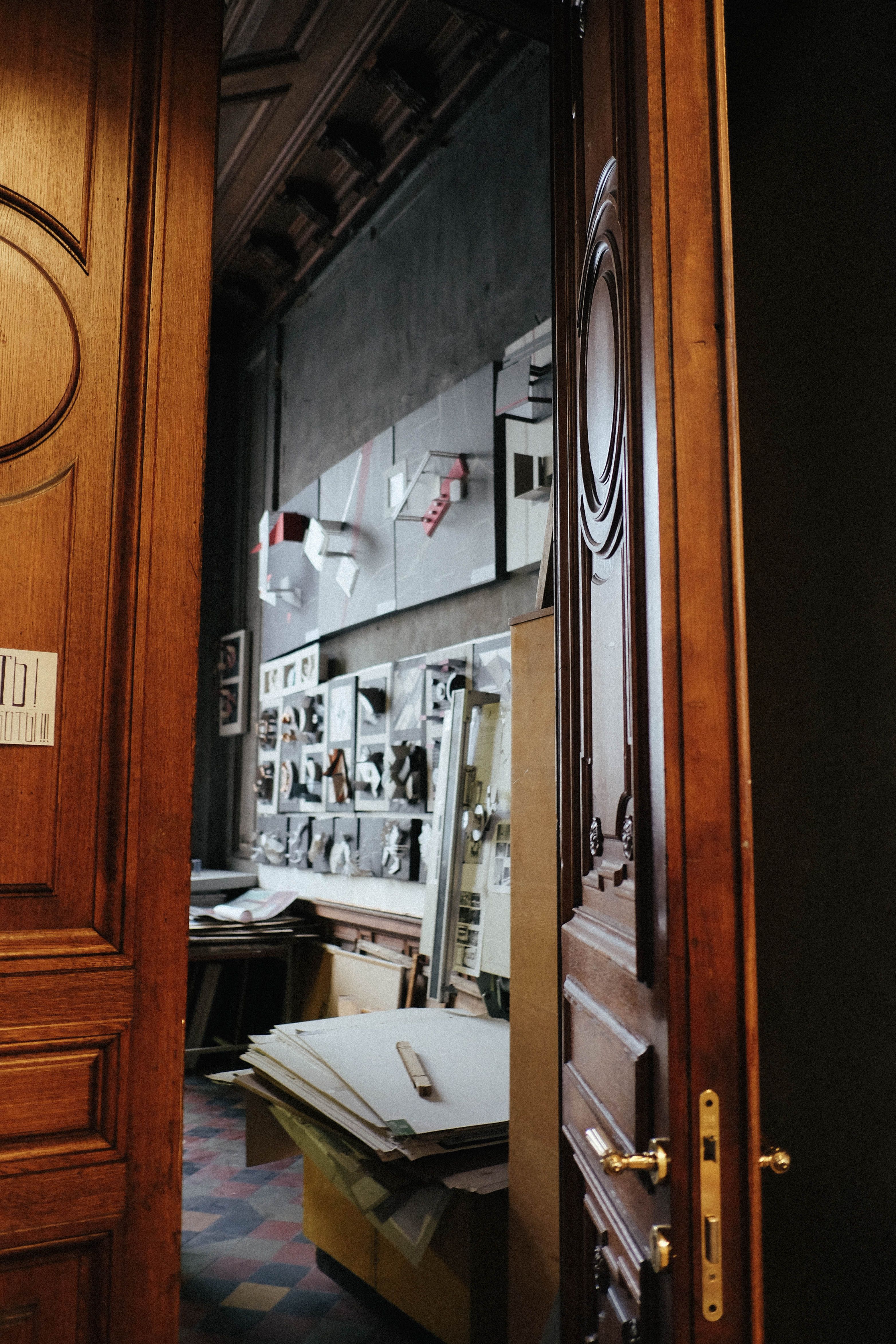 Wooden door and interior of aged classroom with images on wall near artist tools in Academy of Arts