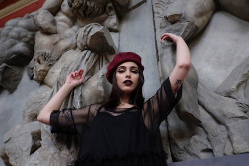 Free From below of young elegant woman with makeup in trendy outfit standing with raised arms near sculptures and looking at camera Stock Photo