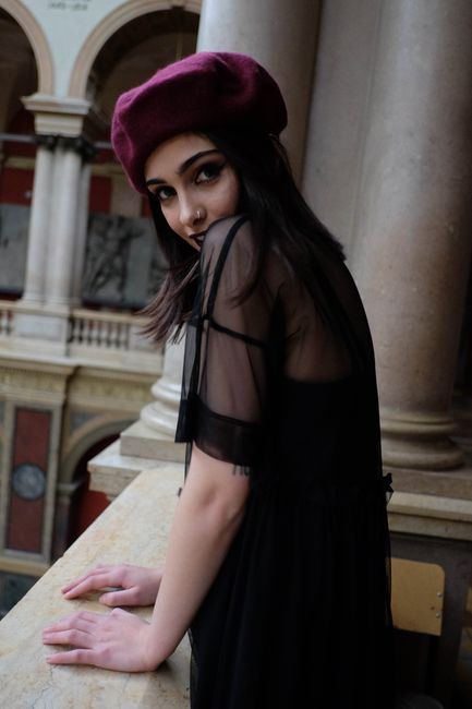 Fotomural Una mujer de moda que lleva una boina y un vestido negro posando elegantemente en el interior junto a un balcón.