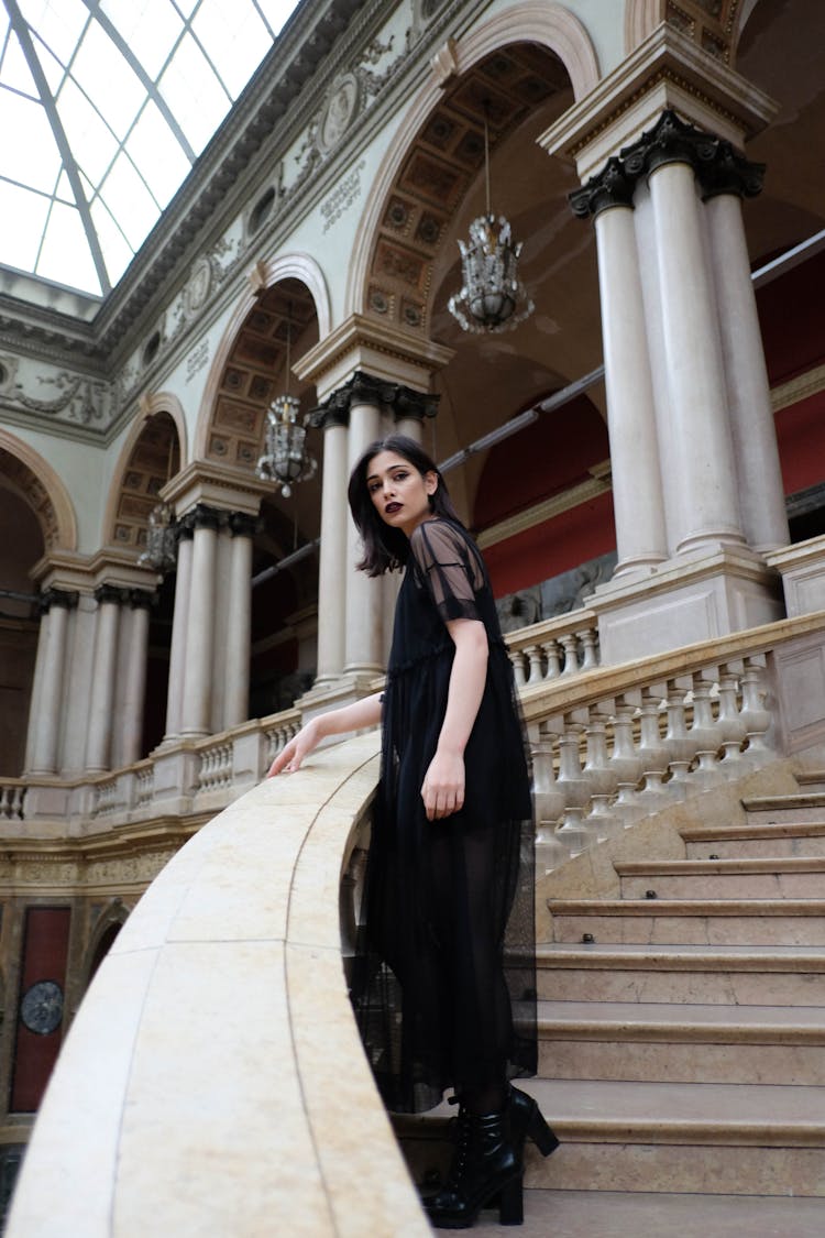 Slim Gothic Woman In Black Dress Standing On Palace Stairs