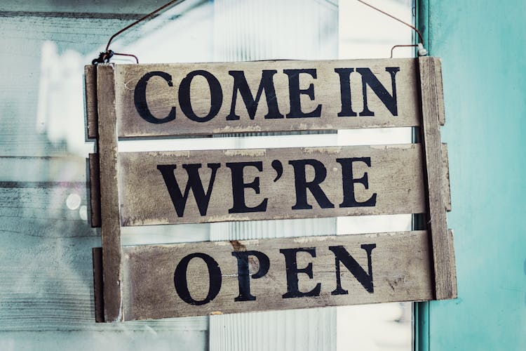 Come In We're Open On A Wooden Sign Hanging On A Door