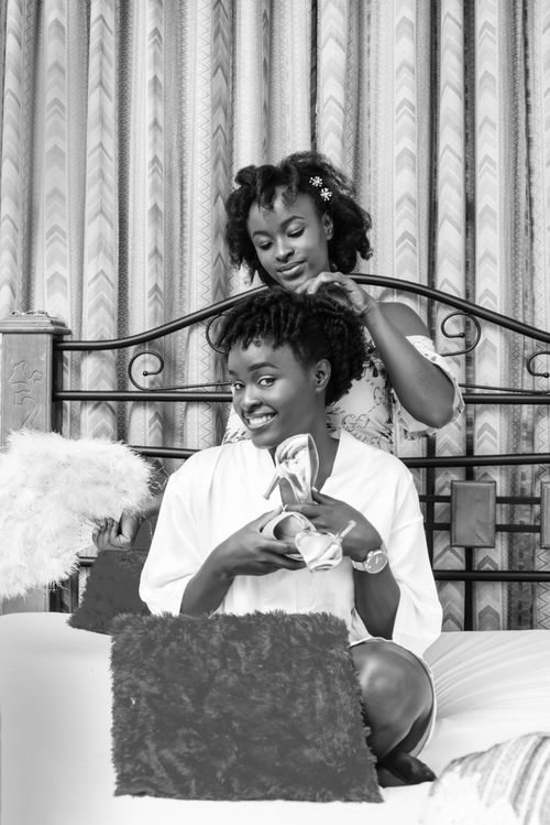 Free Black and white African American female smiling while showing shoes and preparing for marriage ceremony with girlfriend Stock Photo