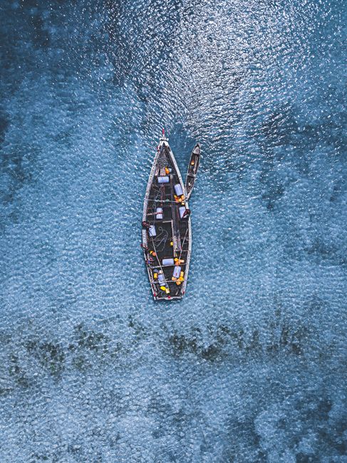 Drone shot of a traditional fishing boat on clear blue ocean water in Zanzibar, Tanzania.
