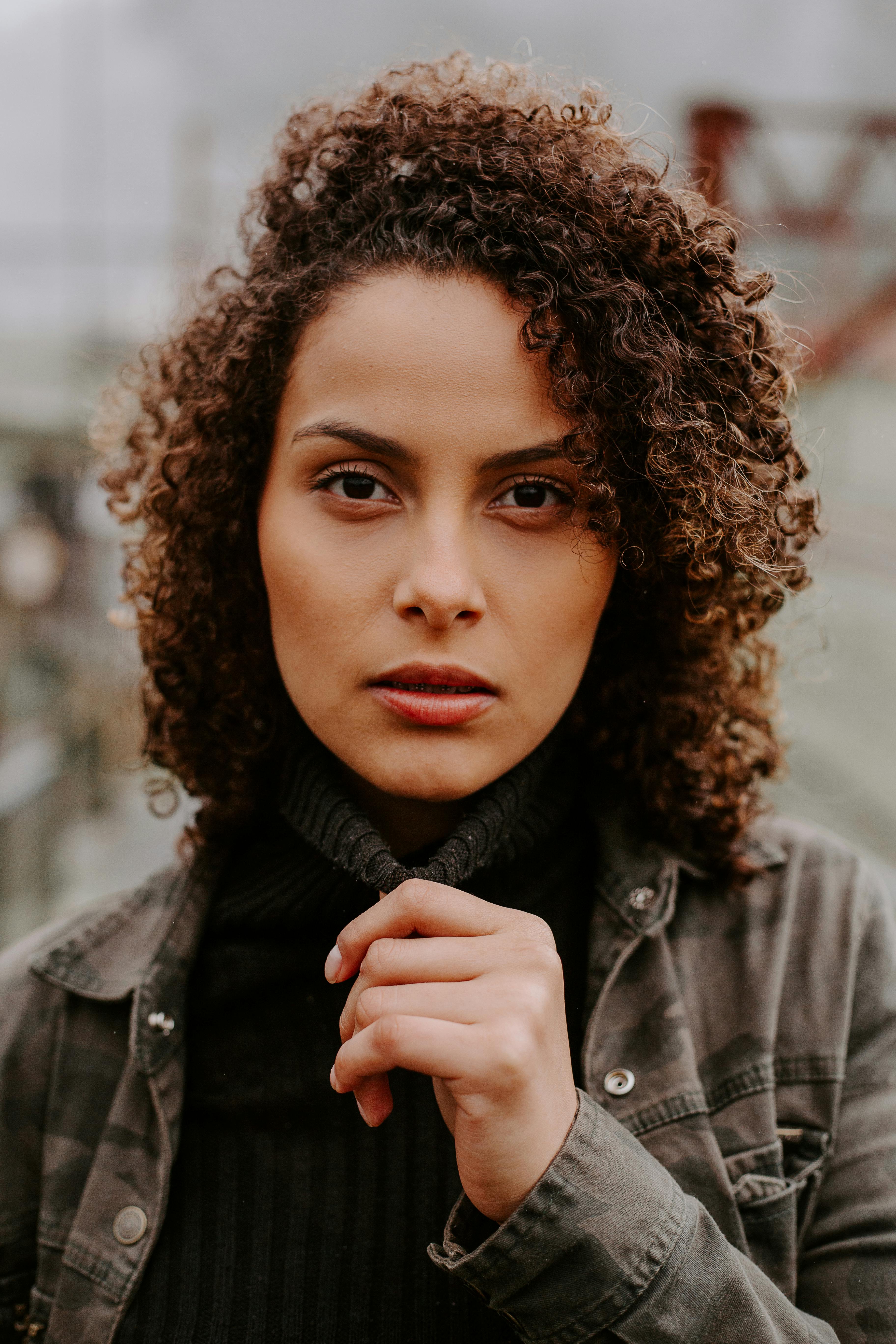 Close-up of a woman with curly hair and a contemplative expression in an urban setting.