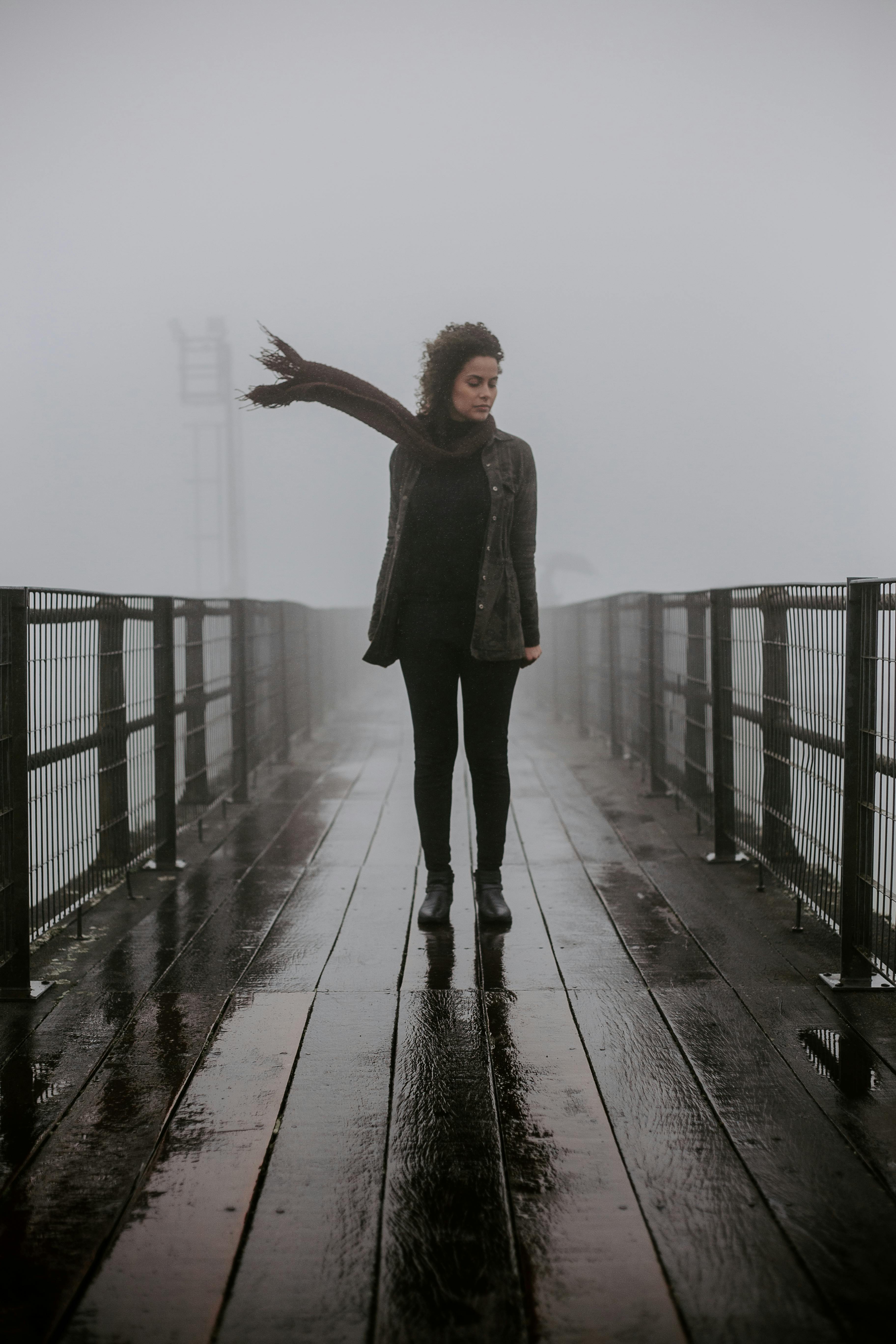 雾气弥漫的桥上，一名身穿黑衣的女子迎风而立，长发飘扬