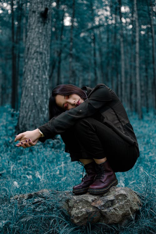 A Woman Wearing a Black Outfit Squatting on a Rock