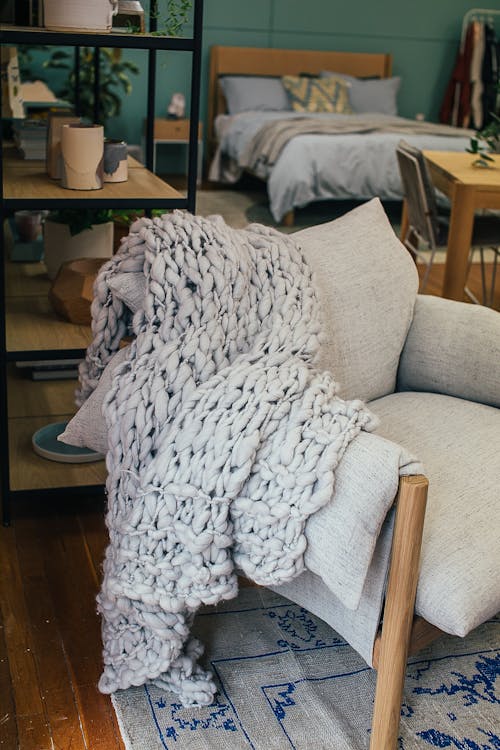 From above of warm knitted blanket placed on comfortable armchair placed near shelf with assorted houseplants in cozy studio apartment in daytime