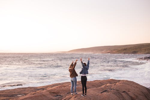 Excited young ladies enjoying sunset over sea with outstretched arms