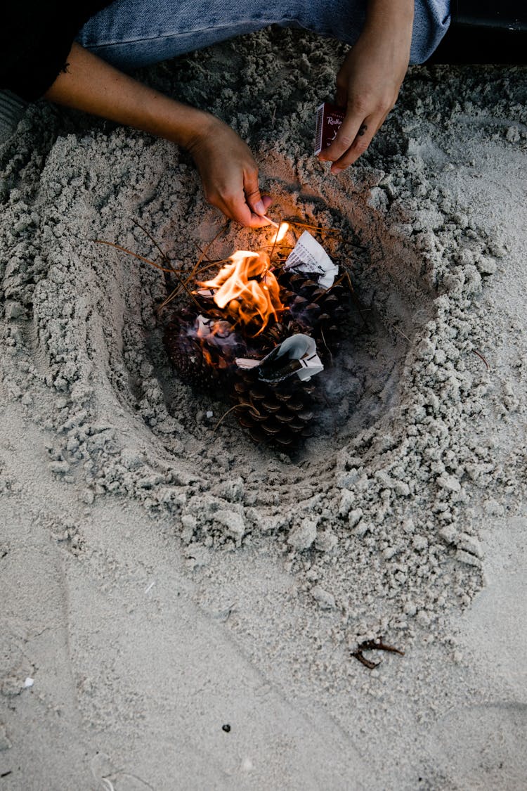 Person Lighting Fire On Sandy Beach