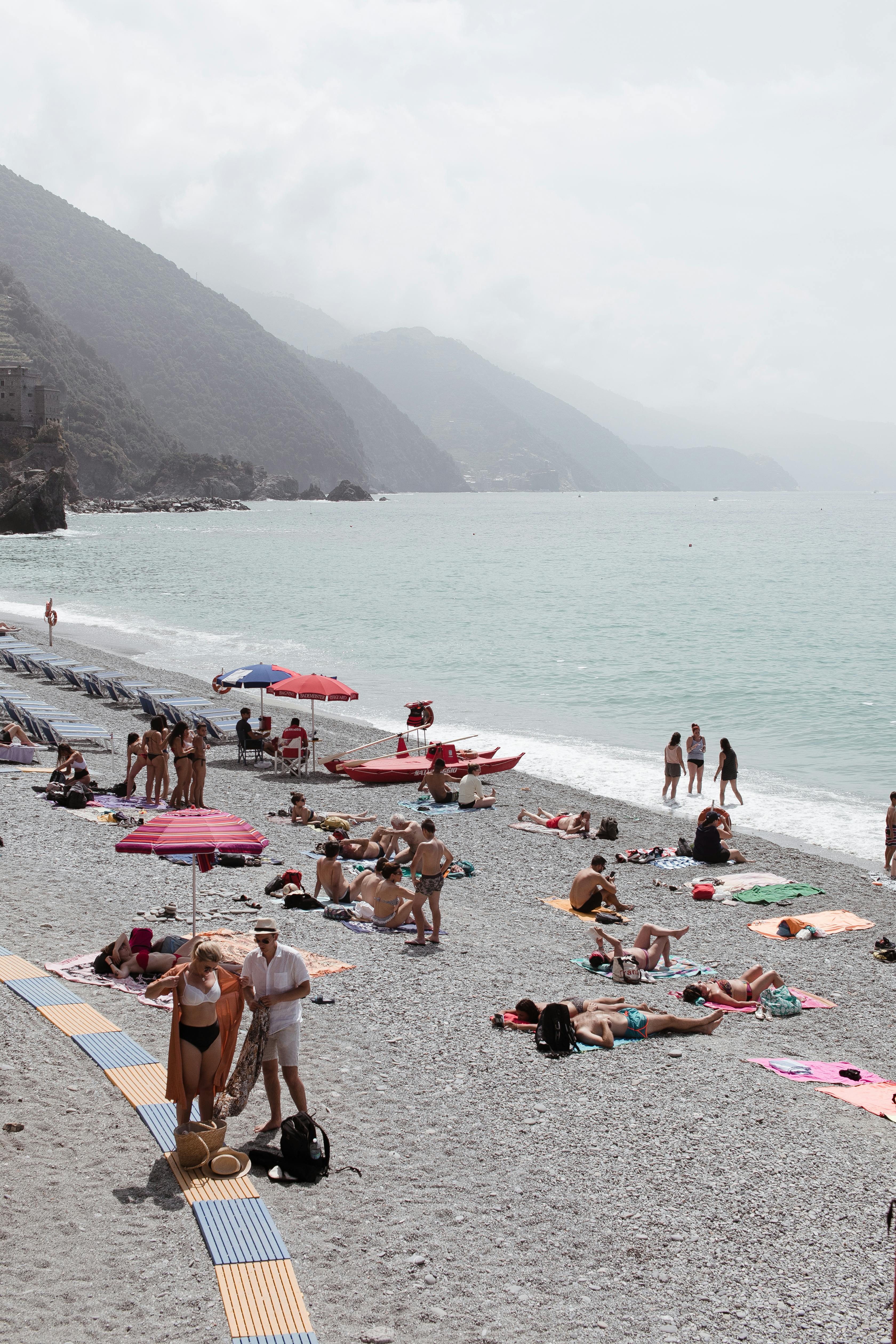 晴天，游客在平静的大海和长满绿色植物的山脉附近的度假海滩上晒日光浴