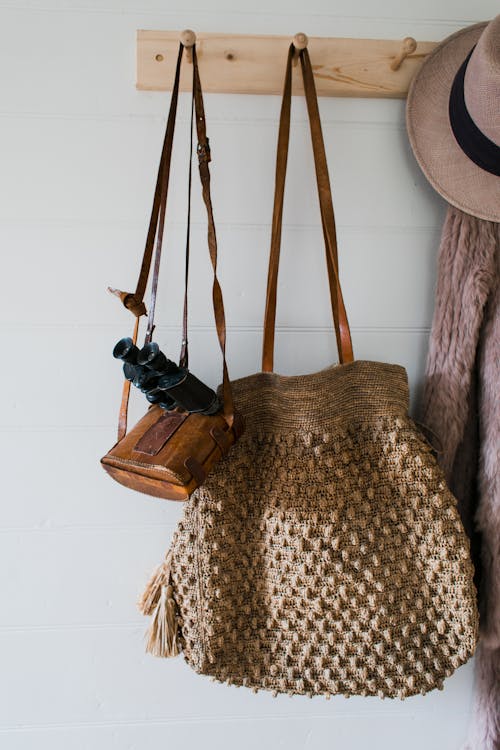 Stylish coat and hat hanging near bag and binoculars on wooden hanger on white wall in apartment