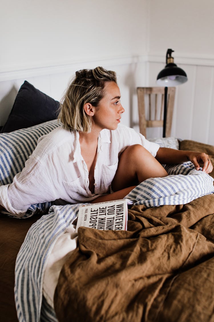 Young Woman With Book In Bed